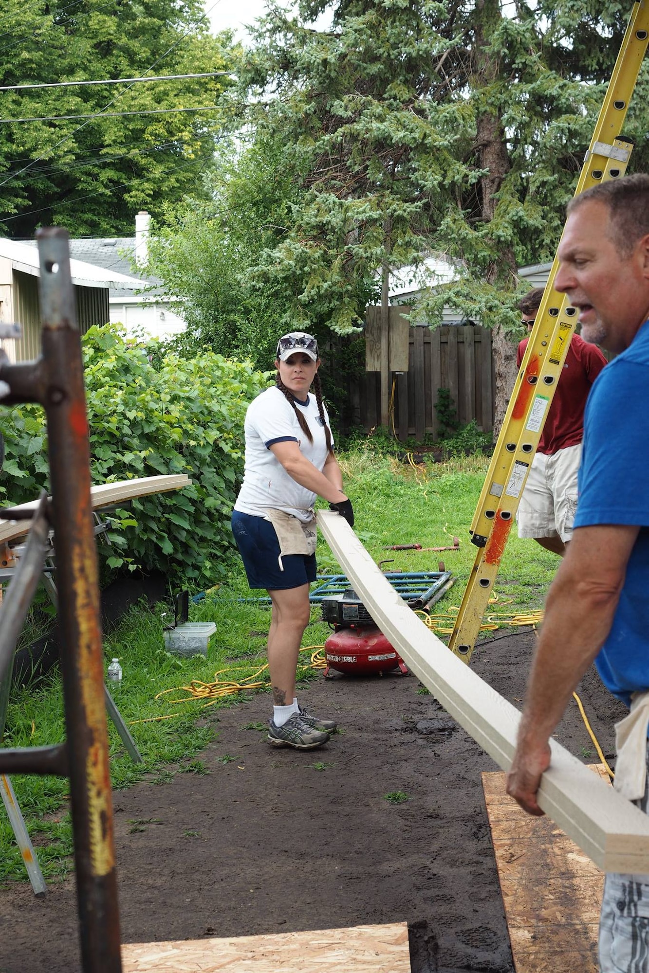 Master Sgt. Erica Hokkanen and Steve Solmonson carry sections of siding trim to the back of the house for installation. 