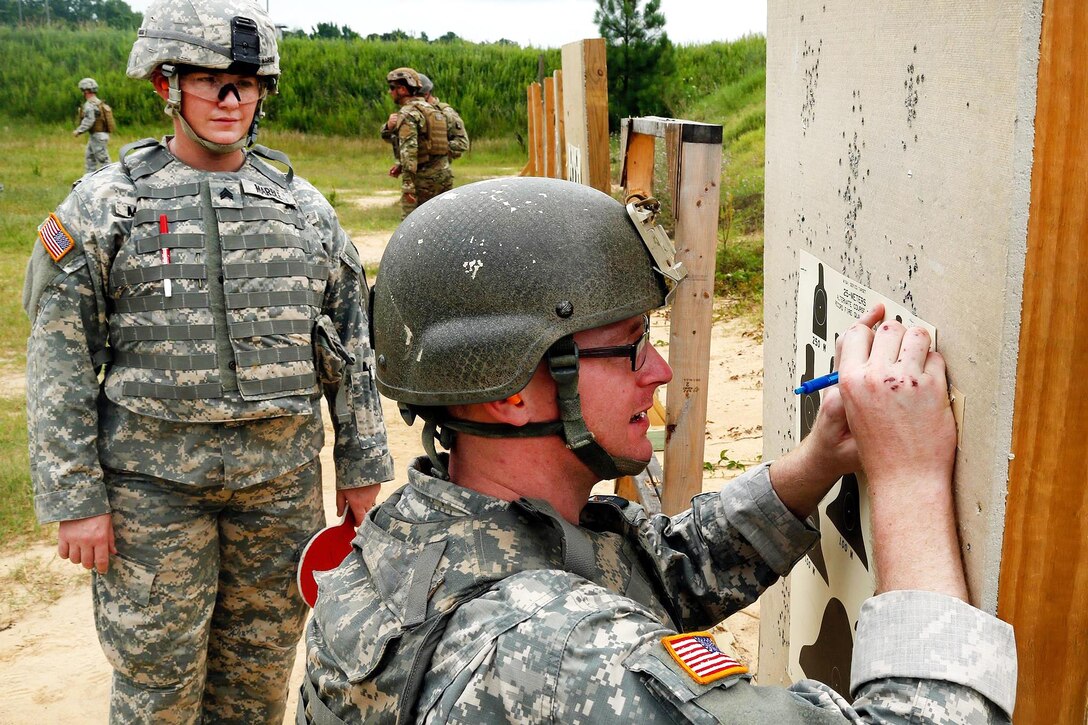 Army Sgt. Ashley Marble, left, observes Spc. Craig Jensen as he writes his name on his qualification target sheet during the Fourth Annual Spc. Hilda I. Clayton Best Combat Camera Competition at Fort A.P. Hill, Va., July 12, 2016. Marble and Jensen are assigned to the 55th Signal Company (Combat Camera). Army Photo by Sgt. Henrique Luiz de Holleben