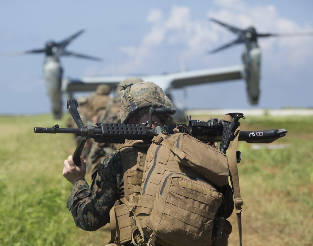 A U.S. Marine trudges toward an Osprey carrying a .50 caliber machine gun after a raid July 2, 2016 at Iejima, Okinawa, Japan. Marines immediately set up security, simulated engaging the enemy and set up a combat operations center after getting off an MV-22B Osprey Tiltrotor Aircraft. They were a part of Golf Company, 2nd Marine Division currently attached to 4th Marine Regiment, 3rd Marine Division, III Marine Expeditionary Force through the unit deployment program. (U.S. Marine Corps photo by Lance Cpl. Amaia Unanue/Released)