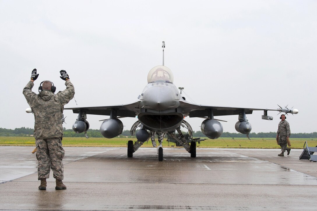 Air Force Master Sgt. John A. Saint George, left, marshals an F-16 Fighting Falcon aircraft into position after landing while a crew chief prepares to chalk the wheels at Papa Air Base, Hungary, July 16, 2016. Saint George is a crew chief and Edwards is a pilot assigned to the Colorado Air National Guard’s 140th Wing. Air National Guard photo by Senior Master Sgt. John Rohrer