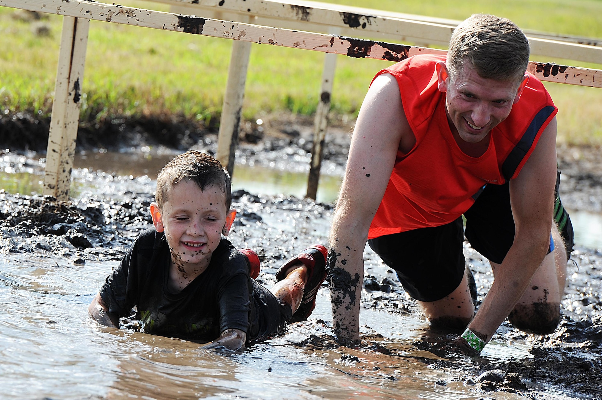 An Airman and his son crawl through the mud during the 2016 Mini Mudder, July 15, 2016 at Minot Air Force Base, N.D. Approximately 900 Airmen and their families attend the event, which lasted 2 hours. (U.S. Air Force photo/Senior Airman Kristoffer Kaubisch)