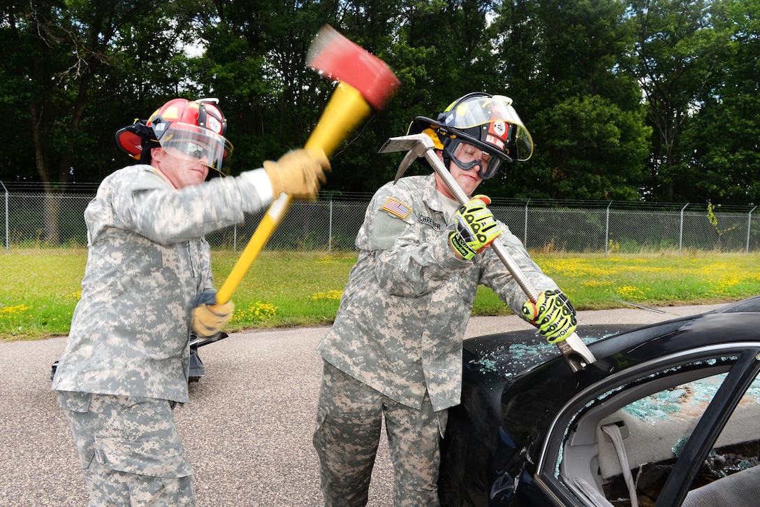 Army Sgt. Somner Goecks, left, swings an ax as Spc. Christopher Schreibner holds a wedge device during vehicle extrication training as part of Patriot North 16 at Volk Field, Wis., July 16, 2016. Goecks and Schreibner are assigned to 826th Ordnance Company. Air National Guard photo by Senior Master Sgt. David H. Lipp