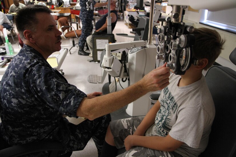 Capt. Mason Philbrook, an optometrist from the Navy Operational Support Center out of Quincy, Mass., gives a young boy an eye exam using a phoropter during the Greater Chenango Cares Innovative Readiness Training event, July 20, 2016.  Greater Chenango Cares is one of the IRT events that provides real-world training in a joint civil-military environment while delivering world-class medical care to the people of Chenango County, N.Y., from July 15-24.
