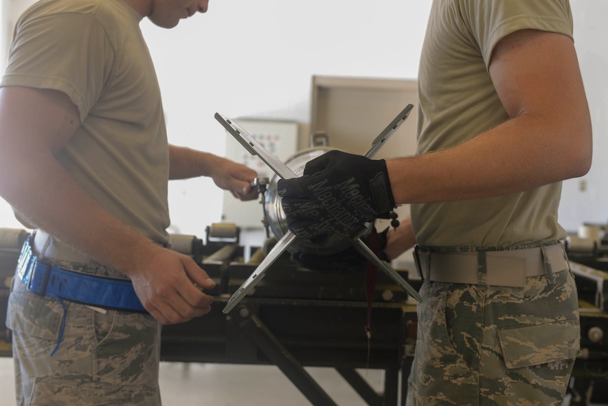 Airmen from the 5th Munitions Squadron, finalize installation of a fin on an inert bomb at Minot Air Force Base, N.D., July 20, 2016. Airmen from the 5th MUNS supply weapons for the B-52 Stratofortress. (U.S. Air Force photo/Airman 1st Class Jessica Weissman)