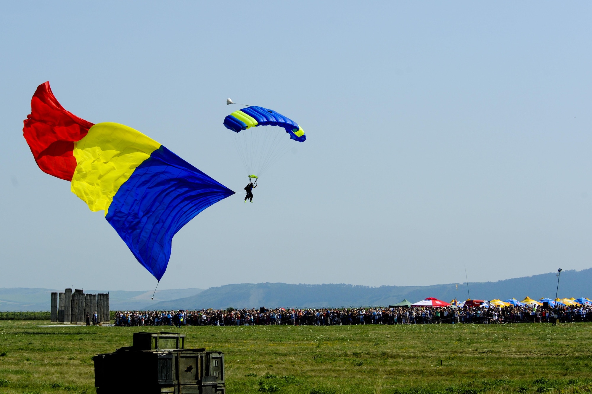 A parachutist floats to the ground while bearing a large Romanian flag before hundreds of spectators during the Romanian air force's 71st Air Base's air show and open house at Campia Turzii, Romania, July 23, 2016. The aviation demonstration took place during the middle of the U.S. Air Force's 194th Expeditionary Fighter Squadron's six-month long theater security package deployment to Europe in support of Operation Atlantic Resolve, which aims to bolster the U.S.'s continued commitment to the collective security of NATO and dedication to the enduring peace and stability in the region. The unit, comprised of more than 200 CANG Airmen from the 144th Fighter Wing at Fresno ANG Base, Calif., as well as U.S. Air Force Airmen from the 52nd Fighter Wing at Spangdahlem Air Base, Germany, piloted, maintained and supported the deployment of 12 F-15Cs Eagle fighter aircraft throughout nations like Romania, Iceland, the United Kingdom, the Netherlands, Estonia and among others. The F-15Cs took to the skies alongside the 71st AB's MiG-21 fighter aircraft and Puma helicopters for both the airshow, the second engagement of its kind at Campia Turzii under Operation Atlantic Resolve, and the bilateral flight training, also known as Dacian Eagle 2016. (U.S. Air Force photo by Staff Sgt. Joe W. McFadden/Released)