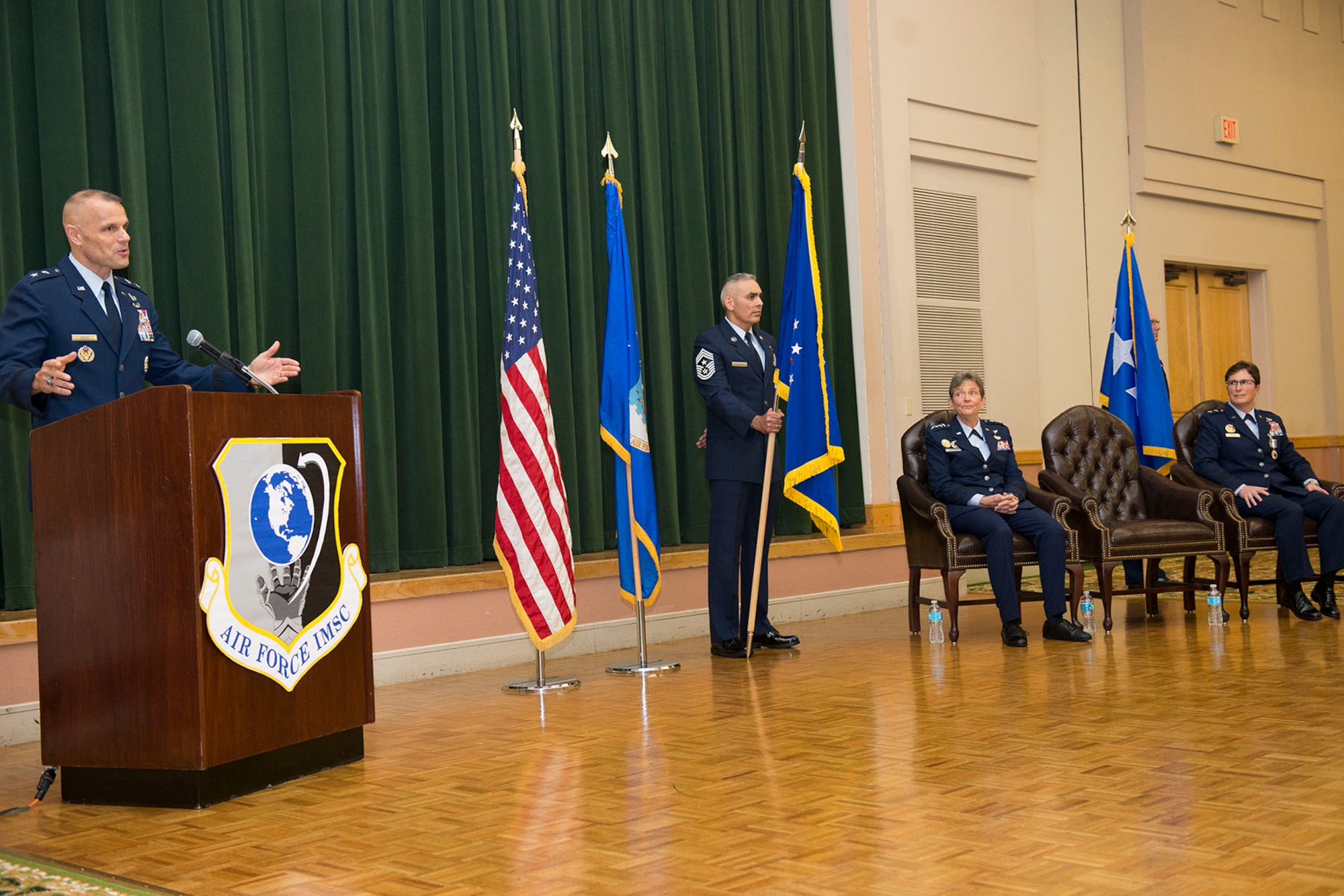 Maj Gen. Bradley Spacy, commander of the Air Force Installation and Mission Support Center, addresses the audience after taking command of AFIMSC July 22 in a ceremony at the Gateway Club, Joint Base San Antonio-Lackland, Texas. Gen. Ellen Pawlikowski, commander of Air Force Materiel Command, and Maj. Gen. Theresa Carter (right), outgoing AFIMSC commander, are seated. Chief Master Sgt. Jose LugoSantiago, AFIMSC command chief master sergeant, holds the unit flag. (U.S. Air Force Photo by Staff Sgt. Marissa Garner)
