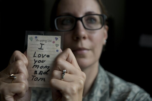 Senior Master Sgt. Janet Lemmons, the 176th Force Support Squadron sustainment and services superintendent, holds up a note her son Tommy wrote to her and his stepfather, Tom, when he was younger. She found the note among a pile of old receipts when she was looking to trade in some diamond earrings after his death. Lemmons tells everyone the note is a thousand times better than diamonds and she keeps it at her desk. (U.S. Air Force photo/Senior Airman Kyle Johnson)