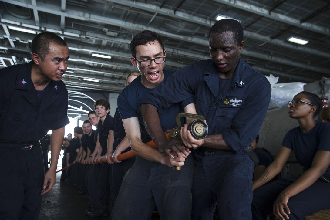 Navy Seaman Cliff Wong, left, relieves the nozzle from Navy Petty Officer 3rd Class Landing Coly during hose-handling training in the hangar bay of the aircraft carrier USS Dwight D. Eisenhower in the Strait of Hurmuz, July 21, 2016. Navy photo by Seaman Apprentice Joshua Murray