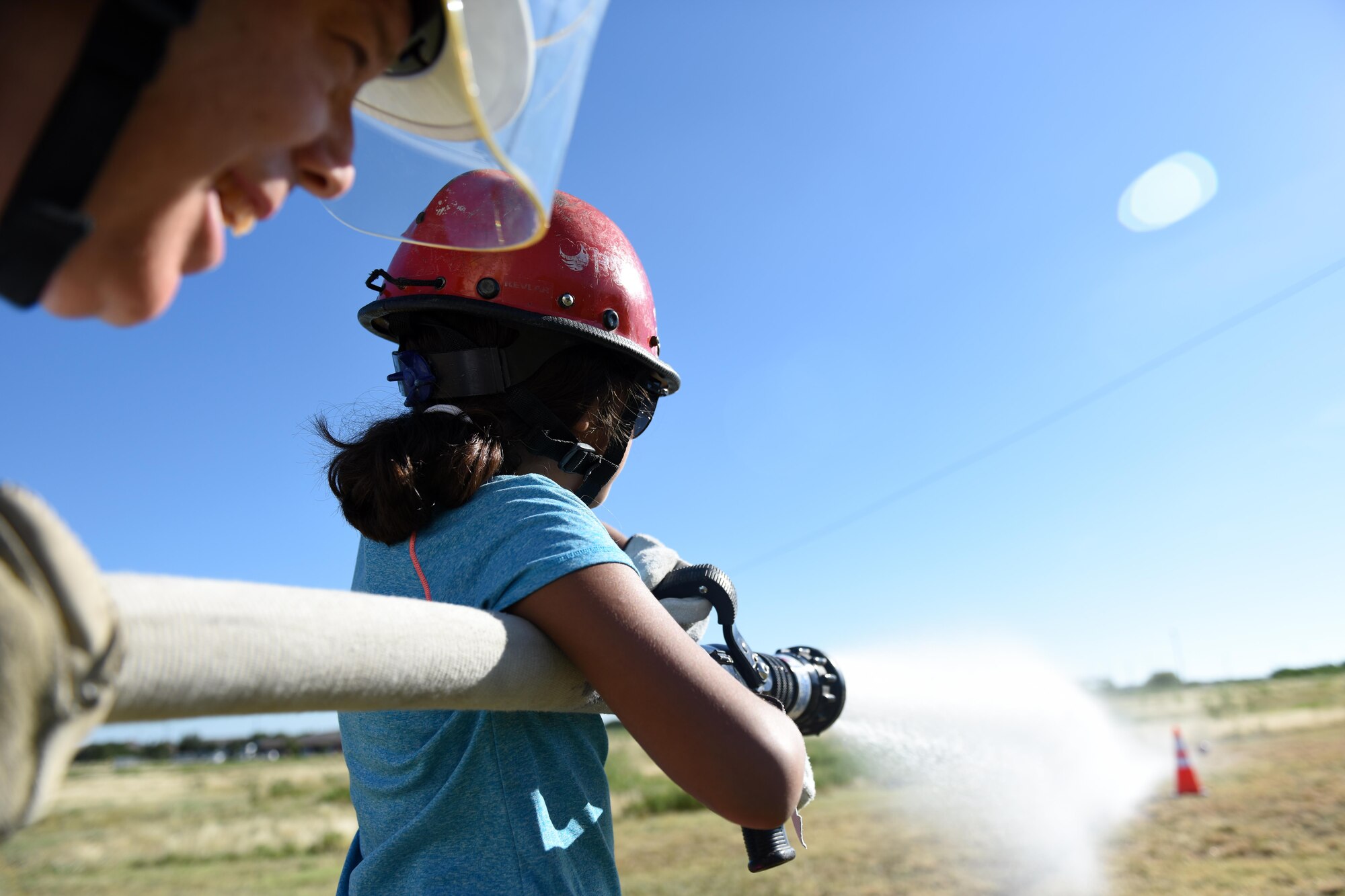 A young girl and Jeff T. Wilkins, Goodfellow Fire Department Chief, spray a target with a fire hose during the Junior Firefighter Camp at the Goodfellow Fire Department, July 20, 2016. Each participant learned how to carry and control a firehose by shooting a soccer ball off a cone. (U.S. Air Force photo by Airman 1st Class Caelynn Ferguson/Released)