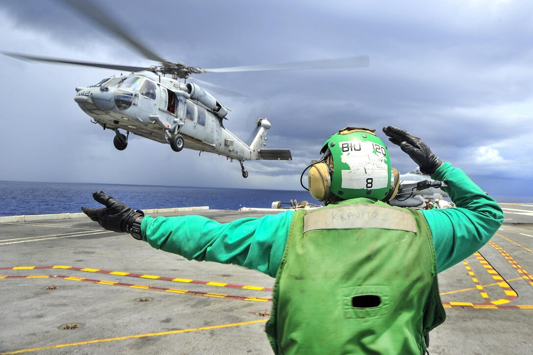A sailor guides an MH-60S Seahawk helicopter on the flight deck of the aircraft carrier USS George Washington in the Atlantic Ocean, July 19, 2016. The helicopter is assigned to Helicopter Combat Support Squadron 28. Navy photo by Seaman Apprentice Krystofer N. Belknap