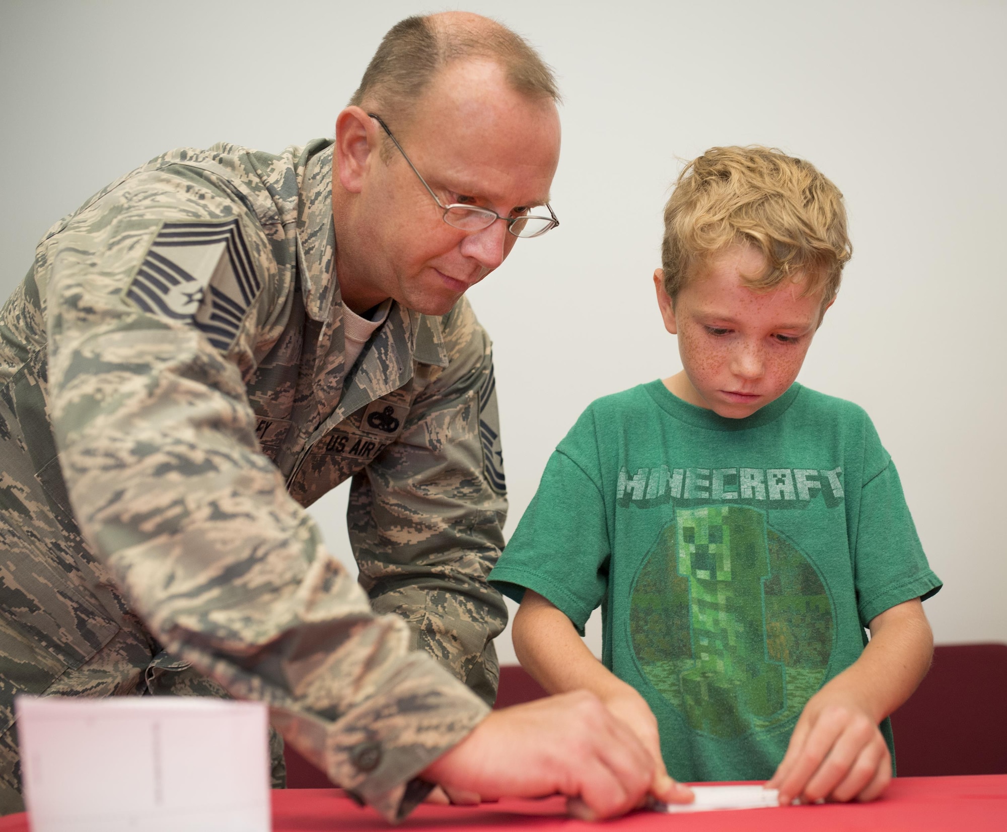 Chief Master Sgt. James Shelley, 33rd Maintenance Group, and his nine-year-old son, Jackson, fold a paper airplane together during a base reading program class July 26 at Eglin Air Force Base, Fla.  The class was taught by Ken Blackburn, Air Force Research Lab Munitions Directorate, who held the Guinness World Record for longest in-air paper airplane flight.  More than 30 kids and parents folded their planes based on Blackburn’s instructions, then filled the base’s digital library with tiny flying paper aircraft.  (U.S. Air Force photo/Samuel King Jr.)