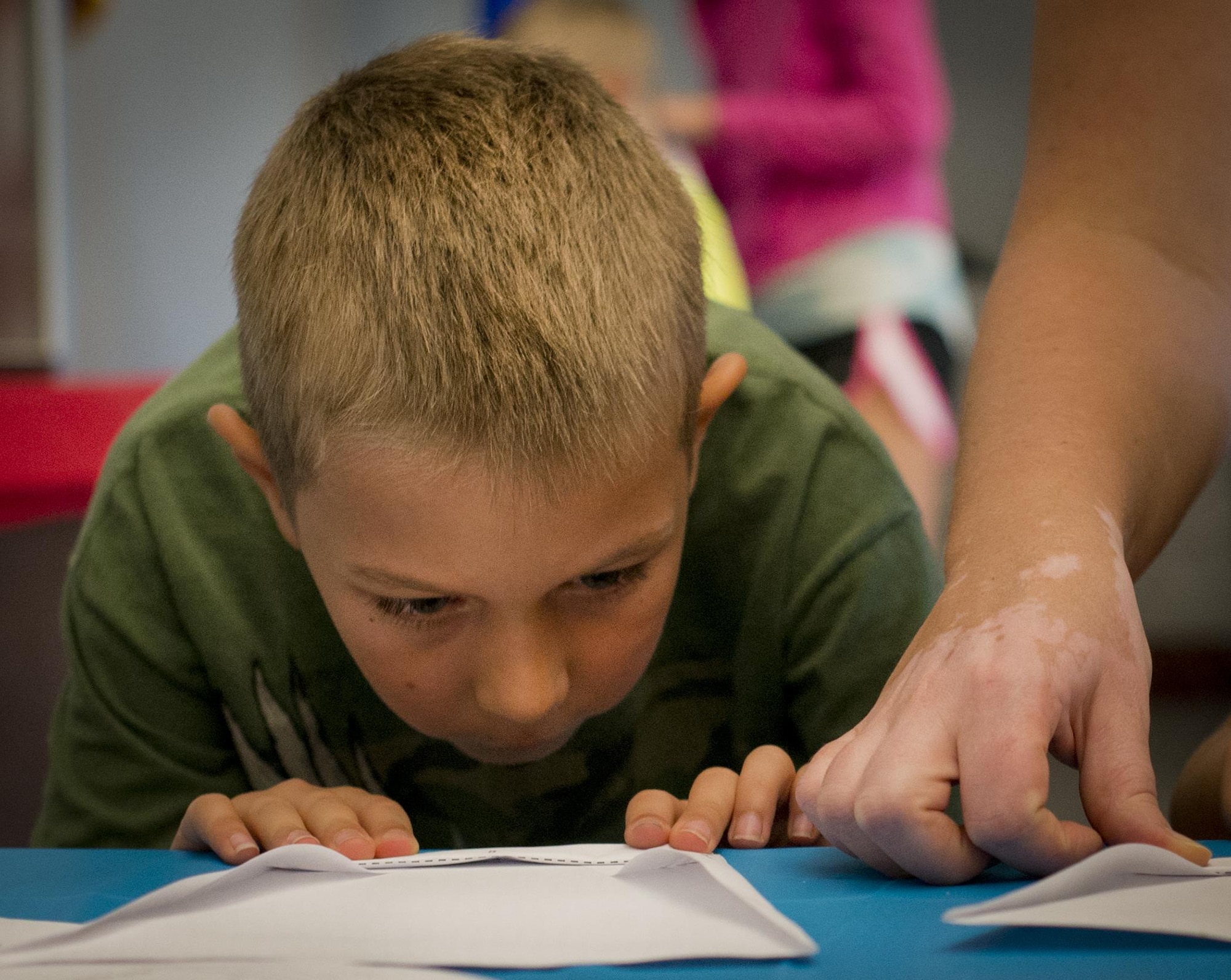 An attendee makes sure his paper airplane fold is “just right” during a base reading program class July 26 at Eglin Air Force Base, Fla.  The class was taught by Ken Blackburn, Air Force Research Lab Munitions Directorate, who held the Guinness World Record for longest in-air paper airplane flight.  More than 30 kids and parents folded their planes based on Blackburn’s instructions, then filled the base’s digital library with tiny flying paper aircraft.  (U.S. Air Force photo/Samuel King Jr.)
