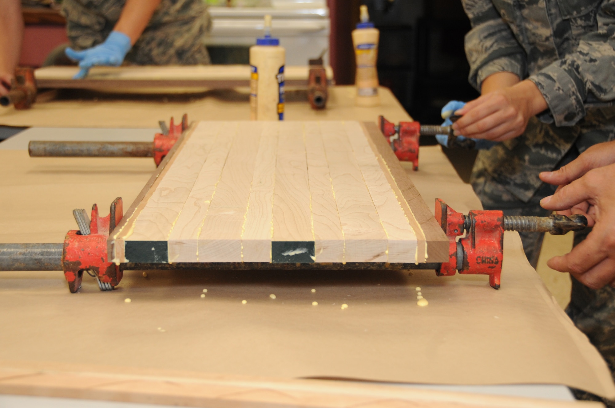 Airmen participating in a wood shop cutting board class use clamps to secure their cutting board so the glue can dry overnight at Barksdale Air Force Base, La., July 18, 2016. The wood shop offers professional instruction on all aspects of woodworking for wood hobbyists. (U.S. Air Force photo/Airman Alexis C. Frost)