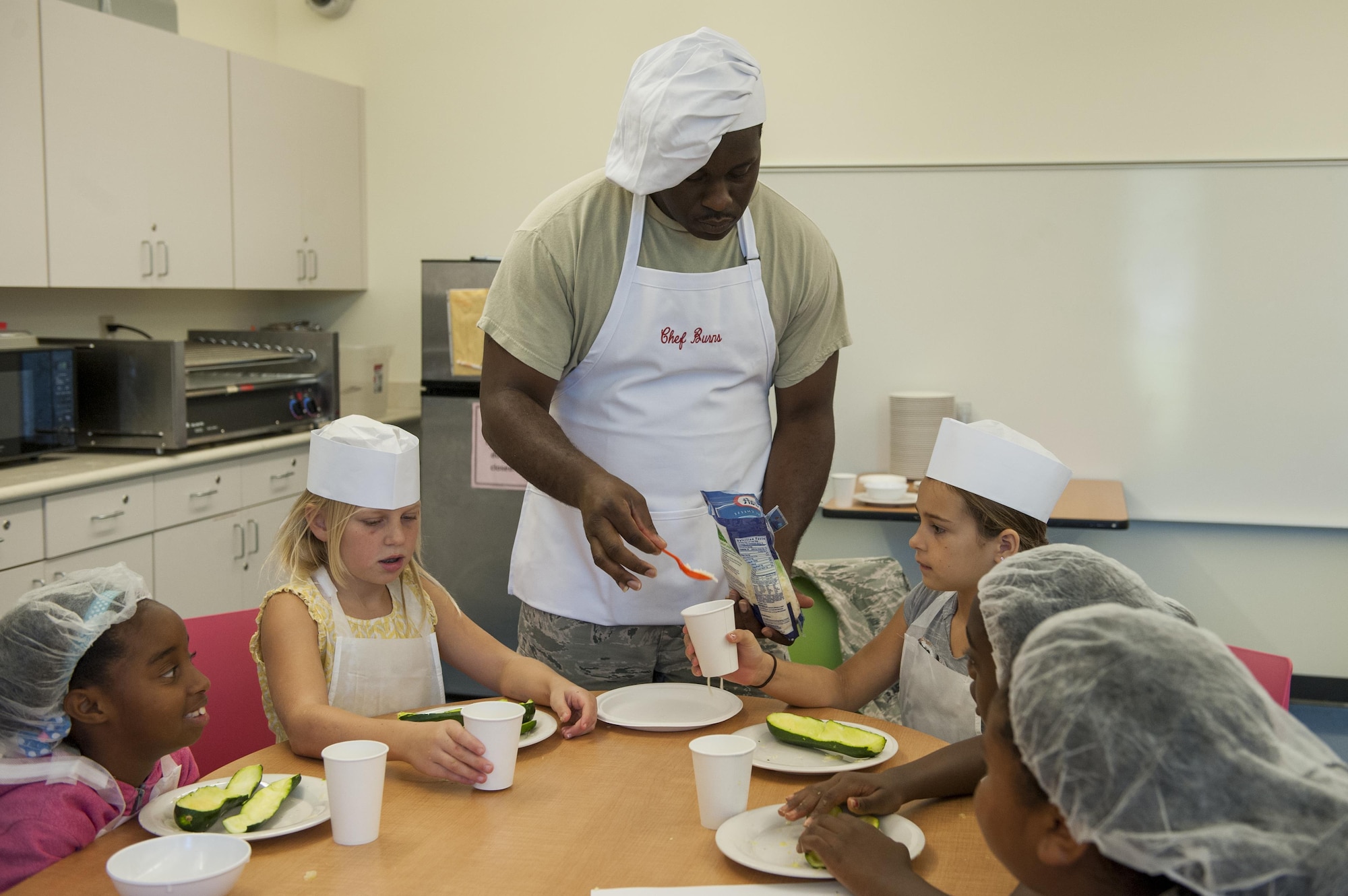 U.S. Air Force Tech. Sgt. Phillip Burns, 23d Civil Engineering firefighter, passes out ingredients to students during a youth cooking camp, July, 26, 2016, at Moody Air Force Base, Ga. On this day of the week-long camp, Burns taught students how to make Italian stuffed zucchini. (U.S. Air Force photo by Airman 1st Class Lauren M. Hunter)