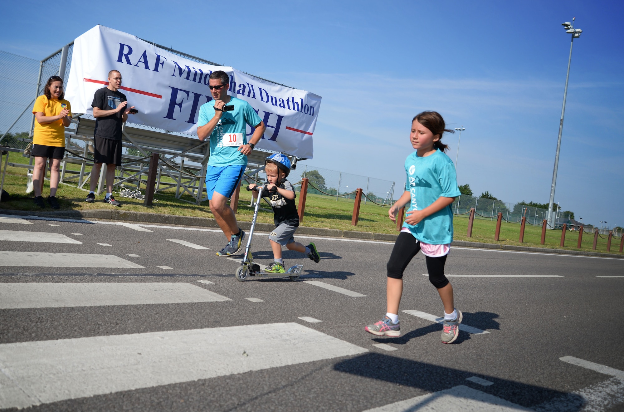 U.S Air Force Maj. Derek Huber, center, 352nd Special Operation Support Squadron flight commander, and youth duathlon participants cross the finish line during the RAF Mildenhall Fitness Center 3rd Annual Duathlon July 23, 2016, on RAF Mildenhall, England. The duathlon is one of several events the fitness center hosts as a way to promote fitness and boost base-wide camaraderie. (U.S. Air Force photo by Senior Airman Christine Halan) 