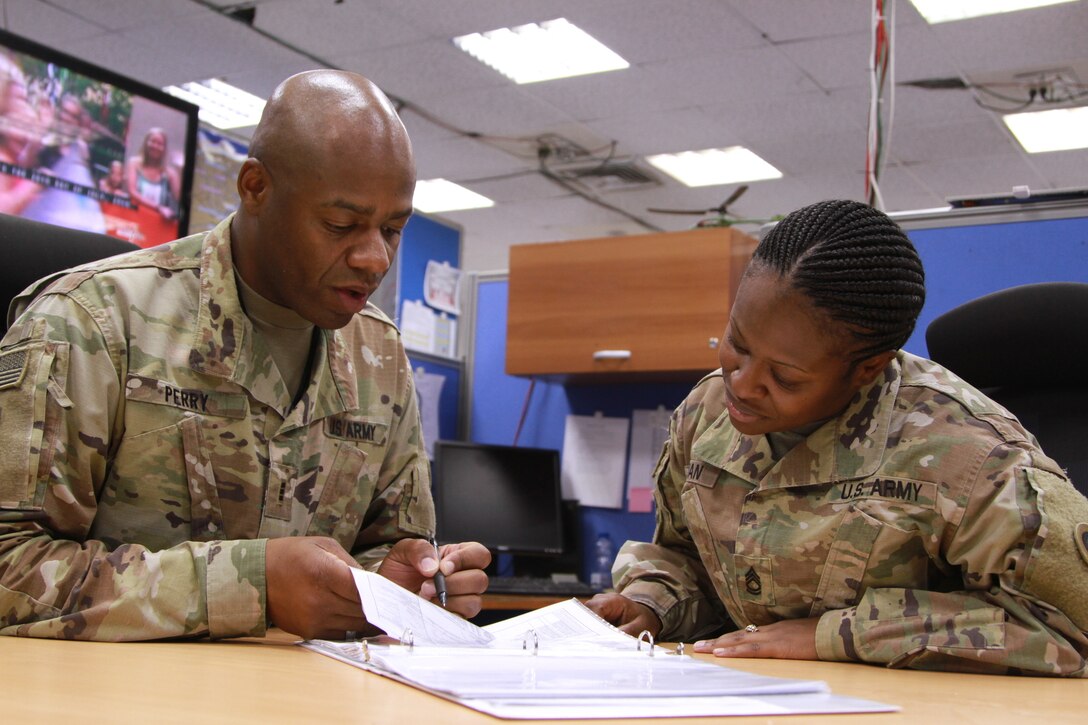 Army Chief Warrant Officer 3 Thomas E. Perry III, mobility officer with the 1st Sustainment Command (Theater), assists Army Sgt. 1st Class Jace V. Morman, sustainment cell noncommissioned officer with the 1st TSC, with her warrant officer packet. (U.S. Army Reserve photo by Sgt. 1st Class Naurys Marte/Released)