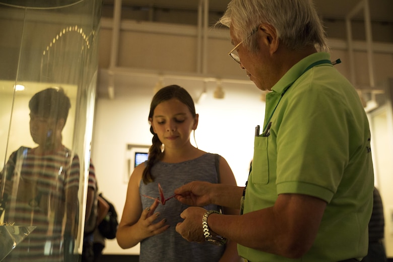 Natalie Kurkierewicz, left, a resident of Marine Corps Air Station Iwakuni, accepts a folded paper crane from a Hiroshima Peace Memorial Museum volunteer during a Marine Corps Community Services trip to Hiroshima Peace Memorial Park, Japan, July 15, 2016. Kikuko Shinjo, better known as ‘Shinjo-Sensei,’ an 89 year-old native of Iwakuni and survivor of the atomic bombing in Hiroshima during World War II, invited a group of MCAS Iwakuni residents to help her donate 1,000 paper cranes, which she folded, to the Children’s Peace Monument at Hiroshima Peace Memorial Park as a symbol for peace. (U.S. Marine Corps photo by Lance Cpl. Donato Maffin)