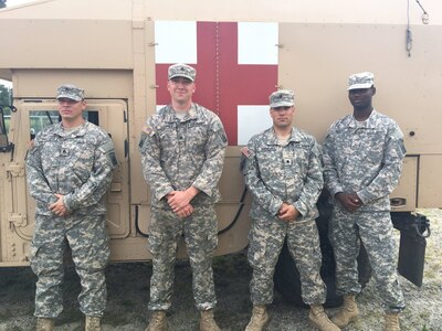 The four Massachusetts Guard members who saved a New Jersey woman from her stranded Cadillac pose in front of an ambulance.