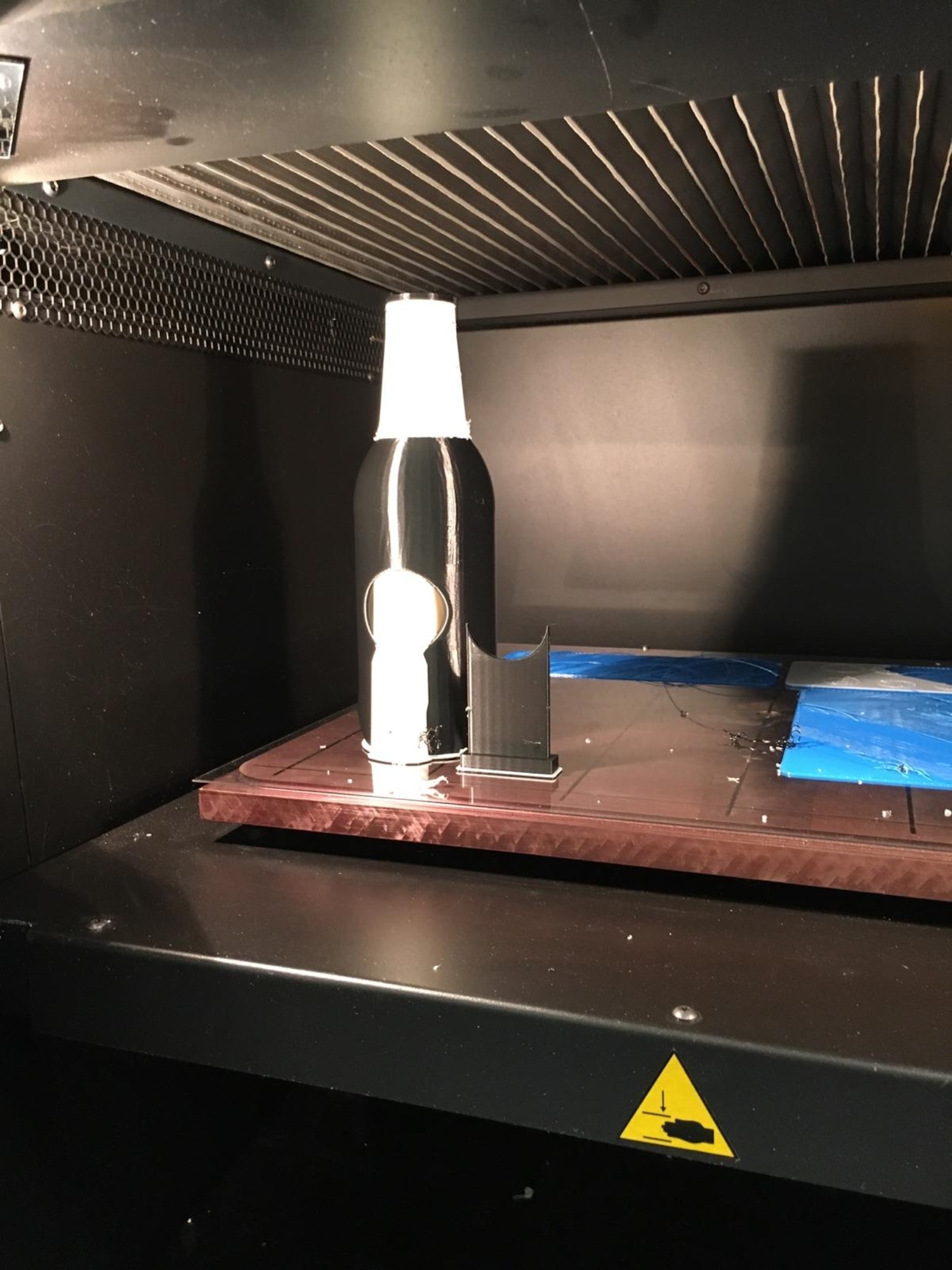 A StrataSys 400mc professional 3D printer prints a soda bottle demonstration piece at AFRL’s Materials and Manufacturing Directorate. The device uses a Fused Deposition Modeling (FDM) 3D printing technology, also called Fused Filament Fabrication (FFF). A thermoplastic filament is pushed and melted through an extruder, to be deposited layer after layer to create a 3D printed part. The device is a similar class of equipment that some on the project team will use. (U.S. Air Force photo/Dennis Butcher)