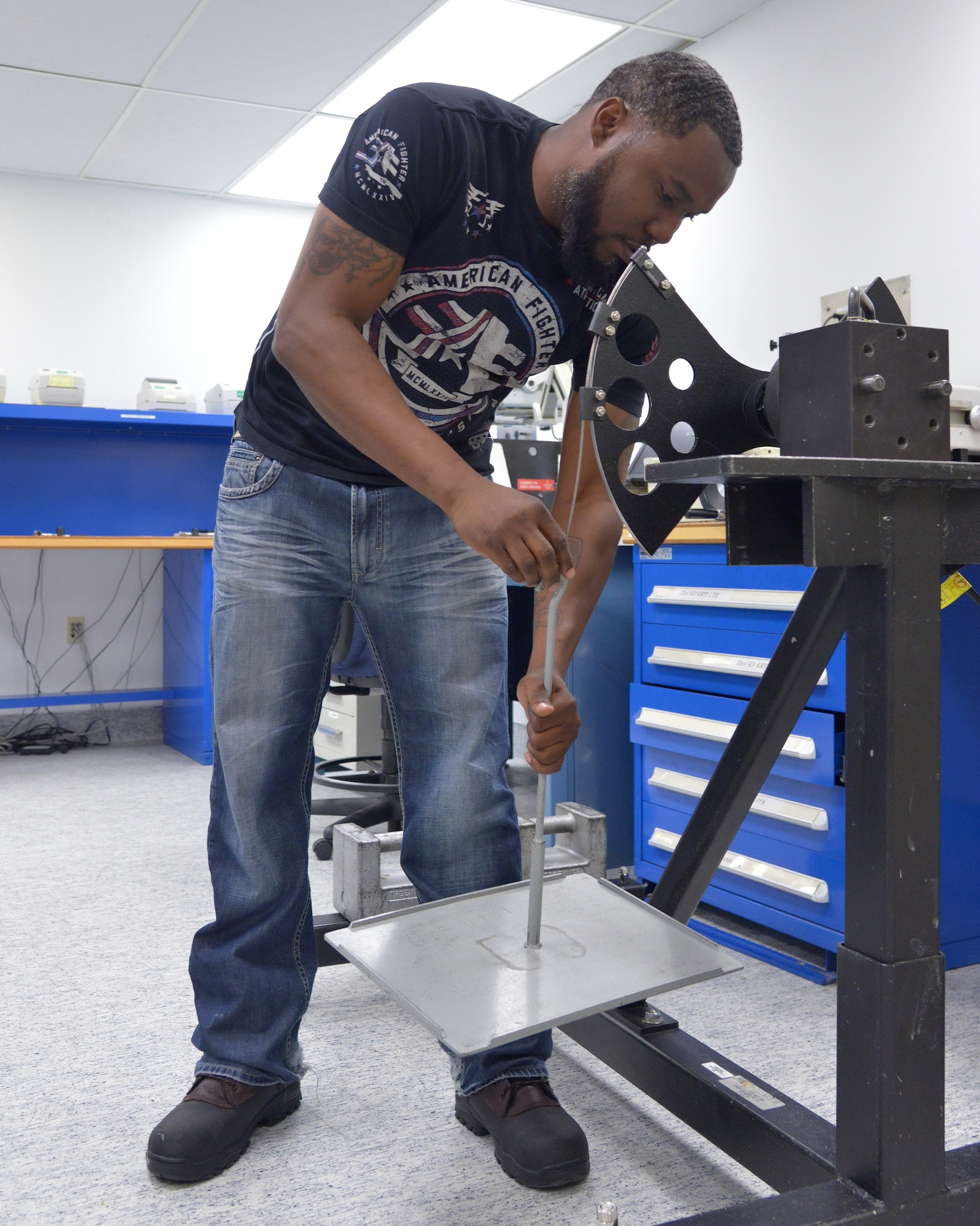 Micah Willis, a technician at the Kirtland Precision Measurement Equipment Laboratory, hangs a weight tray from a calibration arm while calibrating one of the PMEL's torque transducers. (Photo by Jamie Burnett)
