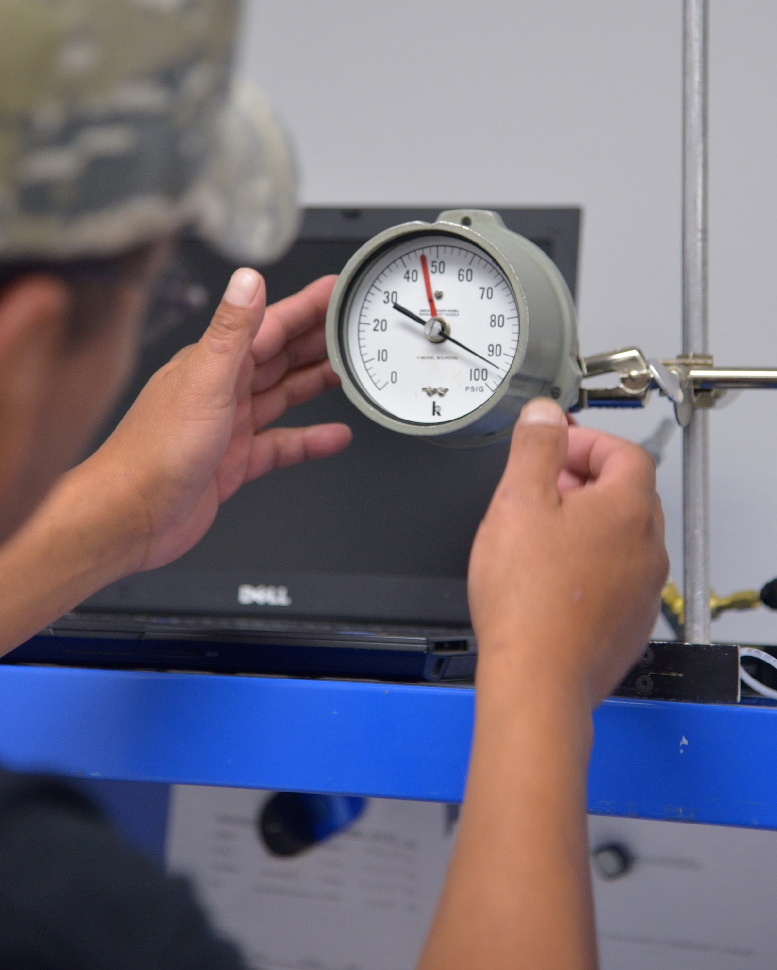 Earl Castillo, a technician in the Kirtland Precision Equipment Measurement Laboratory, taps a pressure gauge to overcome friction error during calibration. (Photo by Jamie Burnett)
