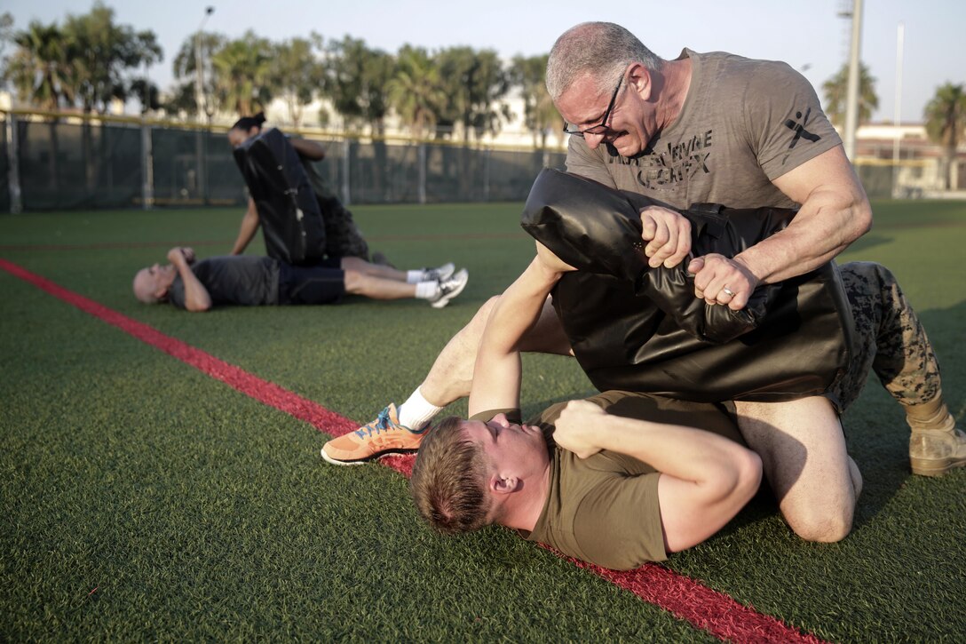 Chef Robert Irvine wrestles with Marine Cpl. Matthew Heldt during a physical training event at Naval Air Station Sigonella, Italy, July 28, 2016. Marines completed a circuit course, which included upper and lower body workouts, and laps around the baseball field, with the celebrity chef. Marine Corps photo by Cpl. Alexander Mitchell
