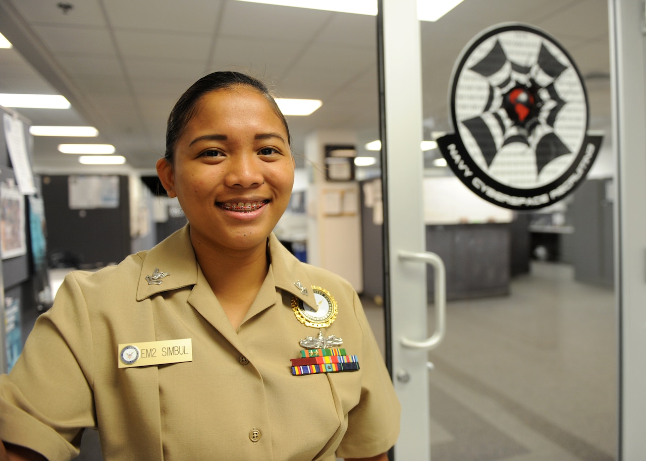 Navy Petty Officer 2nd Class Jhoana Simbul, an electrician’s mate and cyberspace recruiter at Navy Recruiting Command, poses for a photo at the entrance of the Cyberspace Recruiting office in Millington, Tenn., May 20, 2016. In fiscal year 2015, cyberspace recruiting received 66,756 chats, which generated 7,848 leads that ultimately produced 445 new sailors. Navy photo by Petty Officer 3rd Class Brandon Martin