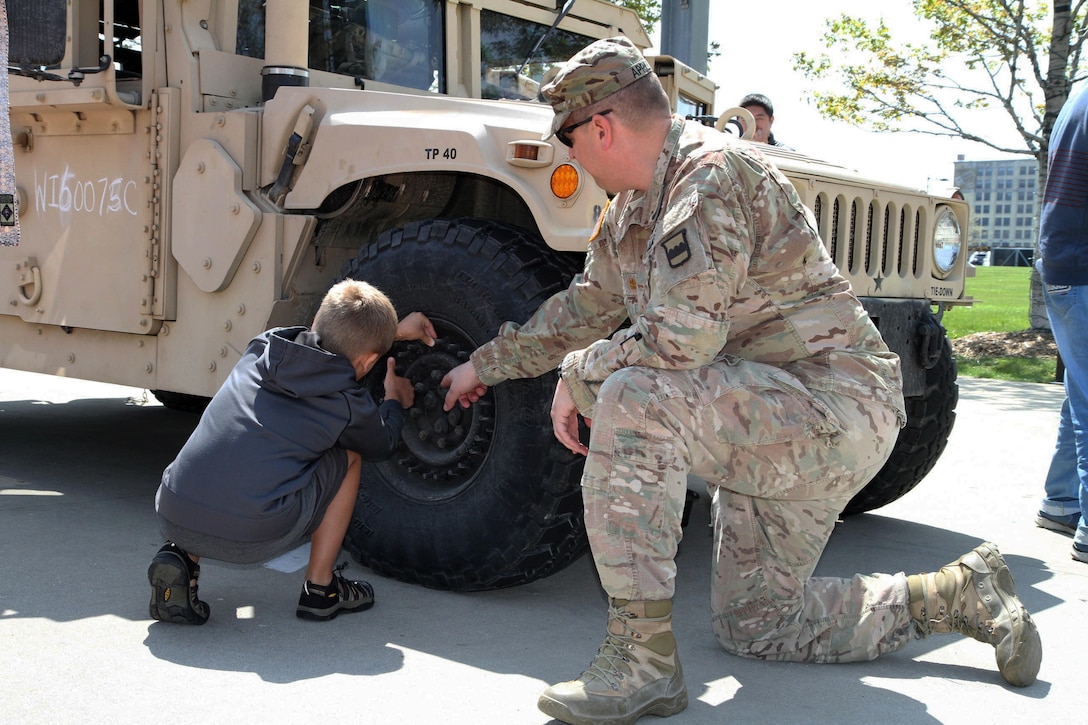 Major Harold Aprill, the executive officer for the 3rd Battalion, 399th Regiment, shows a young boy and his family the durability of a humvee tire during the 2016 Armed Forces Day celebration at the Milwaukee Harley-Davidson Museum, May 21, 2016.  Aprill, who is also a member of the Milwaukee Armed Services Committee, helped organize the event which capped off an entire week of activities for Milwaukee's Armed Forces Week.   Aprill and reservists from the 3/399th, as well as volunteers from the other branches, helped raise military awareness by displaying military vehicles and explaining to civilians their current role in supporting ongoing military efforts around the world. Service members past and present mingled with the crowd throughout the day, a highlight of which was the 13th annual Support the Troops Ride which featured over 300 motorcycle riders.