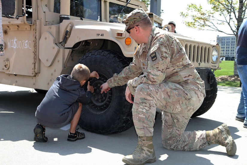 Major Harold Aprill, the executive officer for the 3rd Battalion, 399th Regiment, shows a young boy and his family the durability of a humvee tire during the 2016 Armed Forces Day celebration at the Milwaukee Harley-Davidson Museum, May 21, 2016.  Aprill, who is also a member of the Milwaukee Armed Services Committee, helped organize the event which capped off an entire week of activities for Milwaukee's Armed Forces Week.   Aprill and reservists from the 3/399th, as well as volunteers from the other branches, helped raise military awareness by displaying military vehicles and explaining to civilians their current role in supporting ongoing military efforts around the world. Service members past and present mingled with the crowd throughout the day, a highlight of which was the 13th annual Support the Troops Ride which featured over 300 motorcycle riders.