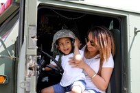 Ryan Cantres of Kenosha, Wis. tries on the U.S. Army's Advanced Combat Helmet as he sits on his mother's lap and experiences what it's like to "drive" a military fire truck during the 2016 Armed Forces Day celebration at the Milwaukee Harley-Davidson Museum, May 21, 2016.  Major Harold Aprill, Executive Officer of the 3rd Battalion, 399th Regiment and a member of  the Milwaukee Armed Services Committee, helped organize the event which capped off an entire week of activities for Milwaukee's Armed Forces Week.    Aprill and reservists from the 3/399th, as well as volunteers from the other branches, helped raise military awareness by displaying military vehicles and explaining to civilians their current role in supporting ongoing military efforts around the world. Servicemembers past and present mingled with the crowd throughout the day, a highlight of which was the 13th annual Support the Troops Ride which featured over 300 motorcycle riders.