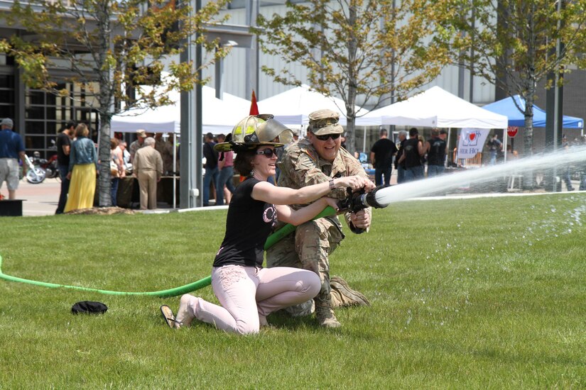 Major Harold Aprill, the executive officer for the 3rd Battalion, 399th Regiment, shows Becca Osmak of St. Francis, Wis. how to properly control the water pressure from a fire hose during the 2016 Armed Forces Day celebration at the Milwaukee Harley-Davidson Museum, May 21, 2016.  Aprill, who is also a member of the Milwaukee Armed Services Committee, helped organize the event which capped off an entire week of activities for Milwaukee's Armed Forces Week.   Aprill and reservists from the 3/399th, as well as volunteers from the other branches, helped raise military awareness by displaying military vehicles and explaining to civilians their current role in supporting ongoing military efforts around the world. Service members past and present mingled with the crowd throughout the day, a highlight of which was the 13th annual Support the Troops Ride which featured over 300 motorcycle riders.
