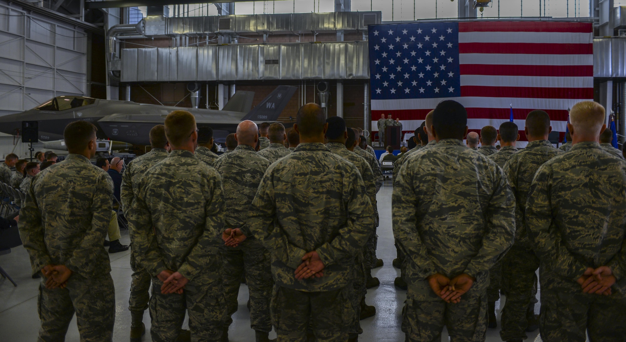 Airmen of the 57th Maintenance Group stand in formation at parade rest during the change of command ceremony in Lightning Aircraft Maintenance Unit hangar at Nellis Air Force Base, Nev., May 26, 2016. During the change of command ceremony, Col. Shane Henderson assumed command of the 57th MXG from Col. Mark Rose at the Lightning Aircraft Maintenance Unit hangar on Nellis AFB. (U.S. Air Force photo by Airman 1st Class Kevin Tanenbaum)