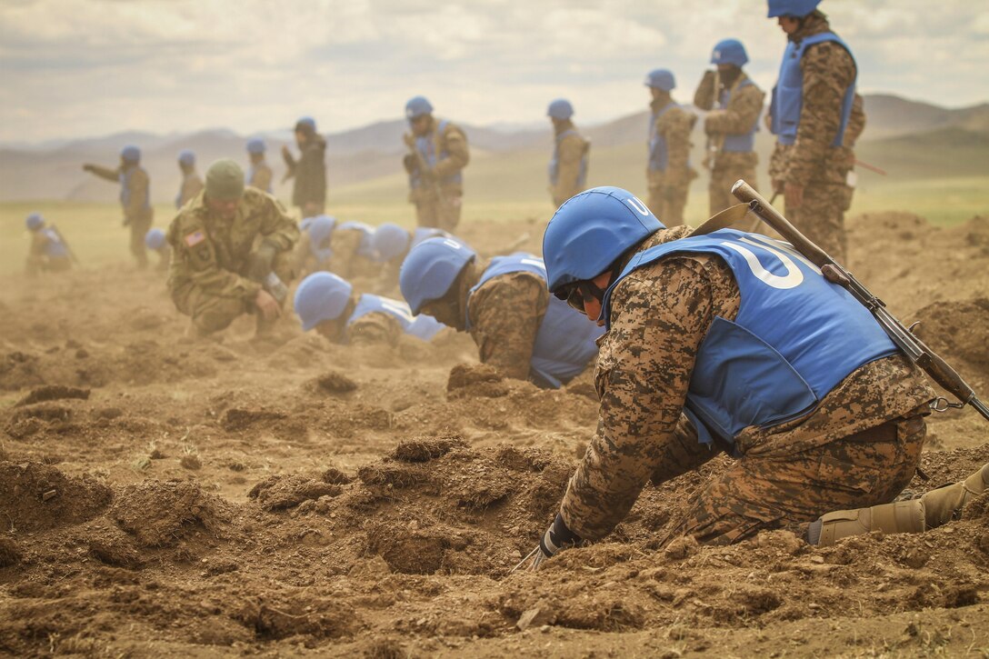 A U.S. service member assists Mongolian soldiers as they search for explosives in a simulated minefield during self-extraction training at Khaan Quest 2016, Five Hills Training Area, Mongolia, May 25, 2016. The annual, multinational exercise focuses on peacekeeping operations. Marine Corps photo by Cpl. Hilda M. Becerra