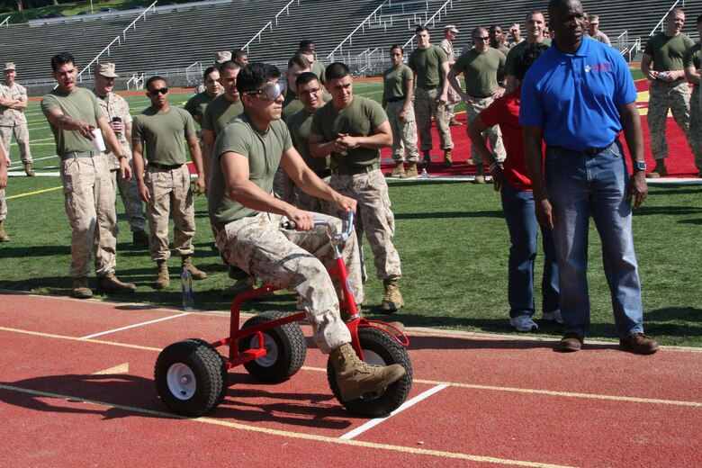 Lance Cpl. Jason Estevez, Combat Visual Information Center, rides a tricycle while wearing a pair of Fatal Vision alcohol impairment simulation goggles, one of the exercises at the 101 Days of Summer field meet May 25. The exercise was meant to give Marines the experience of driving while intoxicated.