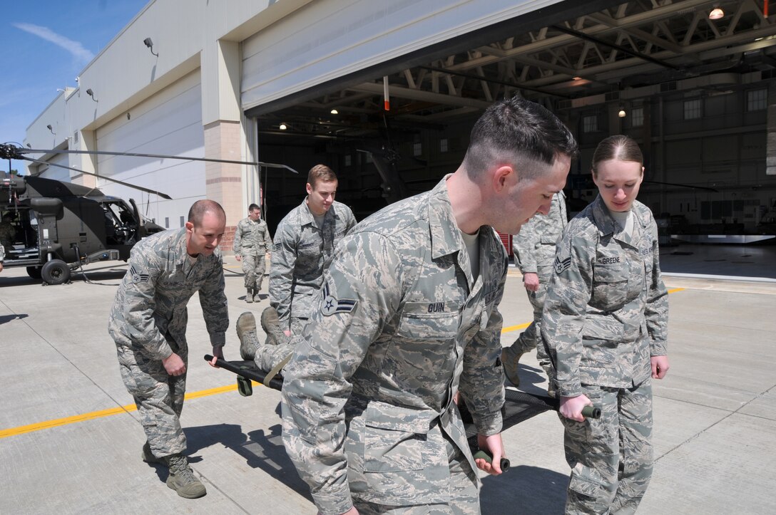 Airman First Class Alan Guin, left front, Senior Airman Courtney Greene, right front, Senior Airman Justin Gilbert, left back, Senior Airman Christopher Iennaco, and Capt. Andrew Christo, right, of the 104th Fighter Wing, 104th Medic Group, train on in flight emergency patient boarding procedures for boarding a HH-60 Medevac aircraft while providing patient care. The Airmen trained on loading and unloading the aircraft with patients prior to practicing with the engines still running on the aircraft, during the Barnes Air National Guard Base Air and Army National Guard Joint Medic augmentee training. (U.S. Air National Guard Photo by Master Sgt. Julie Avey)