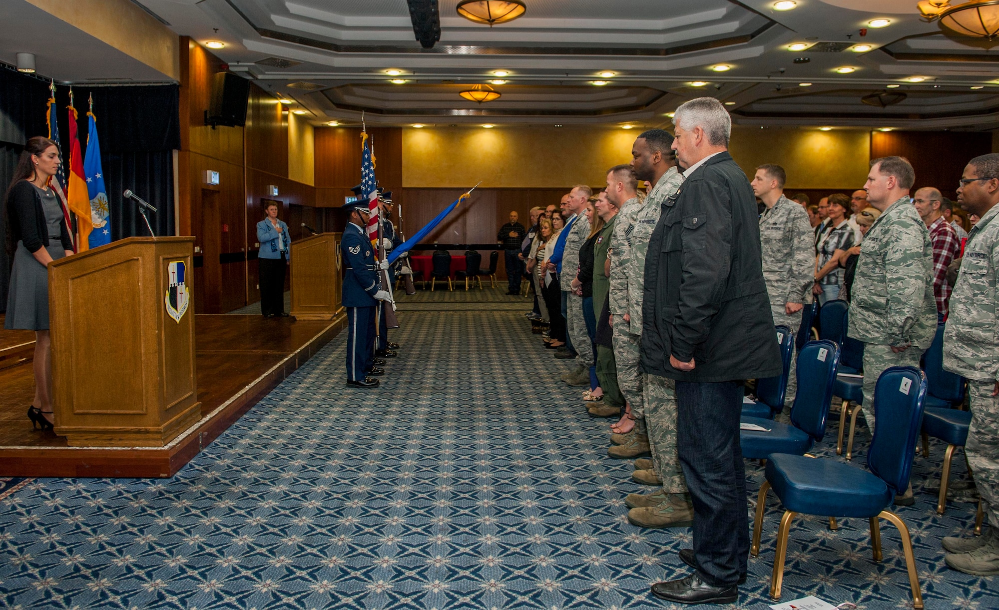 Members of the installation community stand during the presentation of the colors during the Length of Service recognition ceremony in Club Eifel at Spangdahlem Air Base, Germany, June 3, 2016. The installation held the ceremony to thank its civilian work force and their services to the base’s mission. (U.S. Air Force photo by Airman 1st Class Timothy Kim/Released)