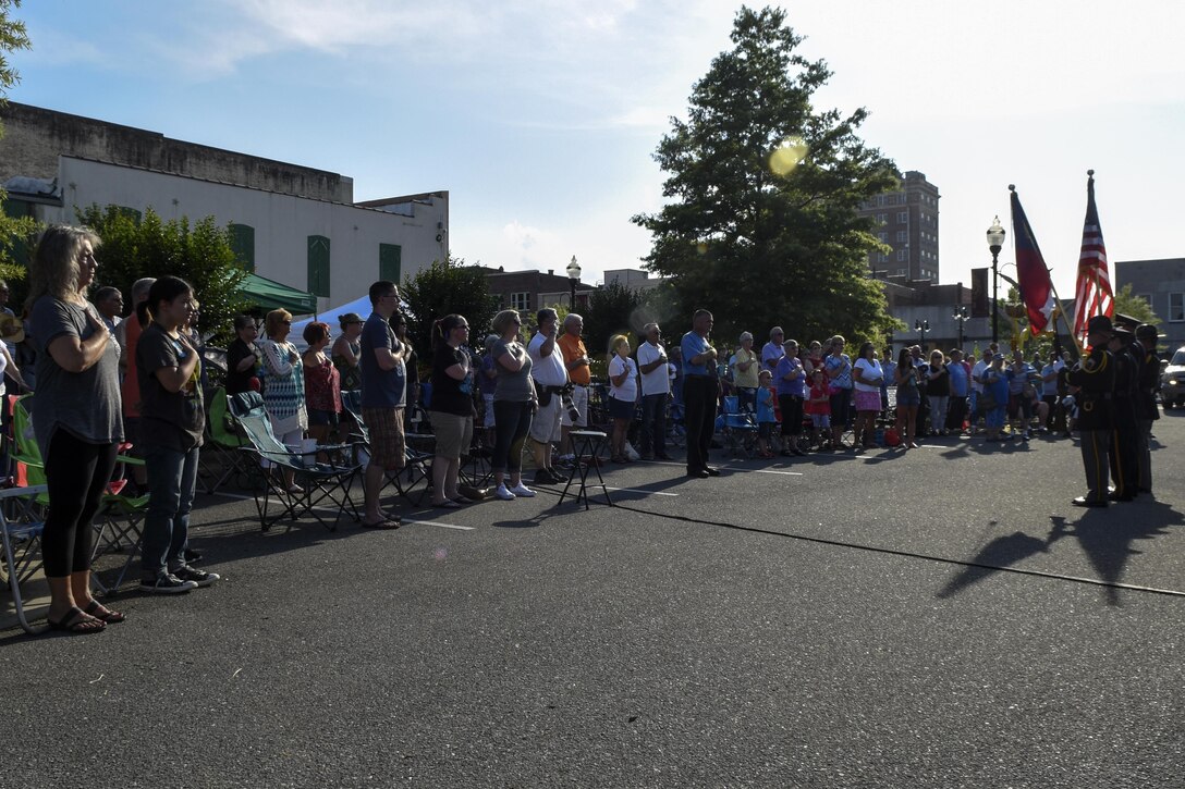 Members of the base and local community stand during the playing of the national anthem and presentation of the colors, June 2, 2016, in Goldsboro, North Carolina. Goldsboro held its military appreciation night during a Center Street Jam event that featured a live band, food trucks, and children’s activities. (U.S. Air Force photo by Airman Shawna L. Keyes/Released)