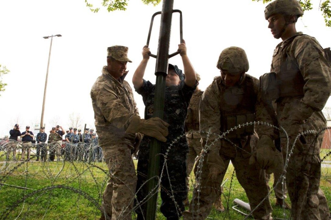 Marines with Alpha 2, Fleet Anti-terrorism Security Team, Marine Corps Security Forces Regiment, assist a U.S. Naval Sea Cadet Corps cadet with setting up concertina wire around a perimeter during a demonstration, April 29, at the Hopkins Hall Gym, at Camp Allen, Virginia. The Marine open house allowed the cadets to get a glimpse at how a Marine or sailor would train with Fleet Anti-Terrorism Security Team. During the tour, the cadets viewed different stations ranging from weapon familiarization to combat life saver displays.  (U.S. Marine Corps photo by Cpl. Jessika Braden/Released)