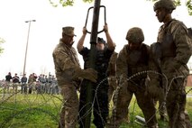 Marines with Alpha 2, Fleet Anti-terrorism Security Team, Marine Corps Security Forces Regiment, assist a U.S. Naval Sea Cadet Corps cadet with setting up concertina wire around a perimeter during a demonstration, April 29, at the Hopkins Hall Gym, at Camp Allen, Virginia. The Marine open house allowed the cadets to get a glimpse at how a Marine or sailor would train with Fleet Anti-Terrorism Security Team. During the tour, the cadets viewed different stations ranging from weapon familiarization to combat life saver displays.  (U.S. Marine Corps photo by Cpl. Jessika Braden/Released)