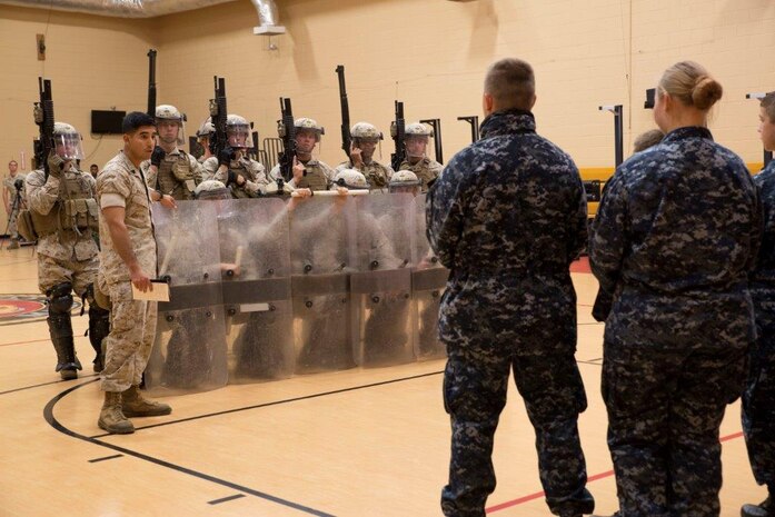 Sergeant Dick J. Moreno explains the importance of working together when in a riot control formation and its purpose, April 29, during a demonstration at the Hopkins Hall Gym on Camp Allen, Virginia. The Marine open house allowed the cadets to get a glimpse at how a Marine or sailor would train with Fleet Anti-Terrorism Security Team. During the tour, the cadets viewed different stations ranging from weapon familiarization to combat life saver displays. Moreno is a Syracuse, N.Y., native and a squad leader with Alpha 2, FAST Company, Marine Corps Security Force Regiment. (U.S. Marine Corps photo by Cpl. Jessika Braden)