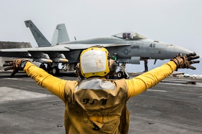 Navy Petty Officer 3rd Class Raimon Hubbard directs an F/A-18E Super Hornet 