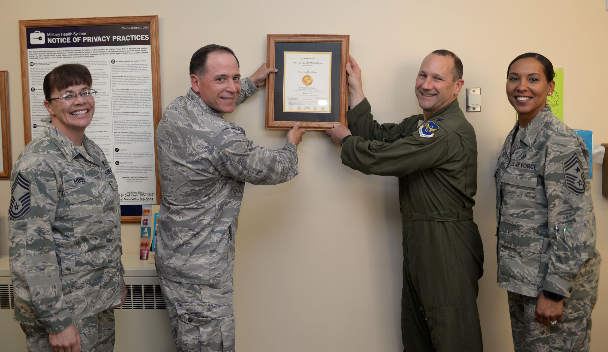 Col. Gentry Boswell, 28th Bomb Wing commander, center right, and Col. Christopher Dun, 28th Medical Group commander, center left, are joined by Chief Master Sgt. Sonia Lee, 28th BW command chief, right, and Chief Master Sgt. Tracy House, 28th MDG superintendent, left, to hang a Joint Commission accreditation certificate in the 28th MDG lobby at Ellsworth Air Force Base, S.D., May 26, 2016. The Joint Commission, an independent, not-for-profit organization, accredits and certifies nearly 21,000 health care organizations and programs in the U.S. Accreditation from the Joint Commission is recognized as a sign of quality that reflects an organization's commitment to meeting certain performance standards. (U.S. Air Force photo by Airman Donald Knechtel/Released) 