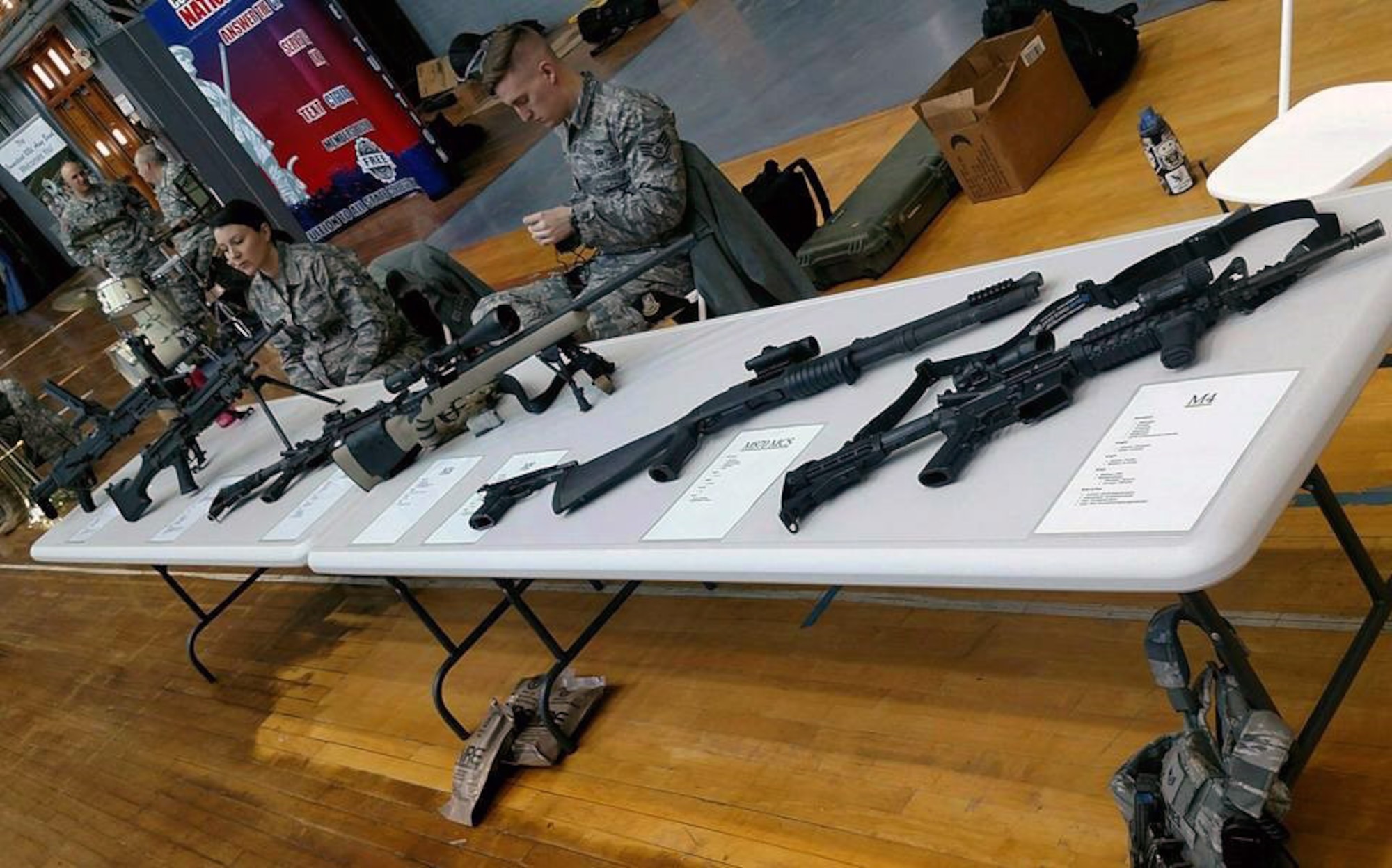 Staff Sergeants Monica Cox and Brandon Gasiorek sit at a weapons display table waiting for a job fair to get underway at the Hartford Armory in Conn. Feb. 27, 2016. (Photo courtesy of Master Sgt. Liz Toth)