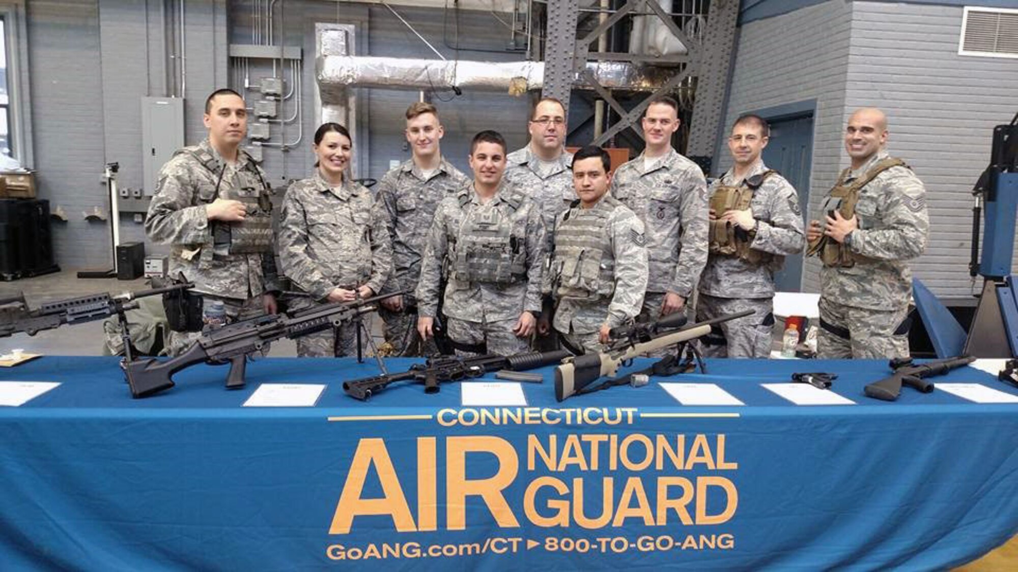 Tech. Sgt. Marvin Perez, Staff Sgt. Monica Cox, Staff Sgt. Brandon Gasiorek, Tech. Sgt. Cody Remy, Senior Master Sgt. Chris Divita, Tech. Sgt. Noah Castro, Staff Sgt. Brian Davies, Master Sgt. Aaron Bowman, and Tech. Sgt. Nick Augelli stand at a weapons display table during a job fair held at the Hartford Armory in Conn. Feb. 27, 2016. (Photo courtesy of Master Sgt. Liz Toth)