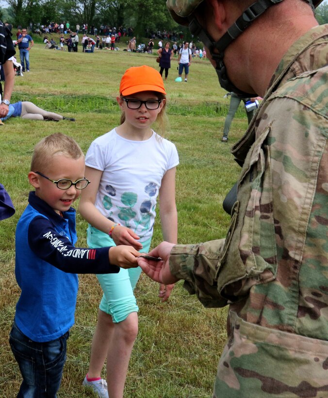Chief Warrant Officer 2 Scott Pfaff gives an 82nd Airborne Division patch to some children after his parachute jump over Sainte Mere Eglise, France to commemorate the 72nd anniversary of D-Day, June 5, 2016. U.S. Army photo by Capt. Joe Bush