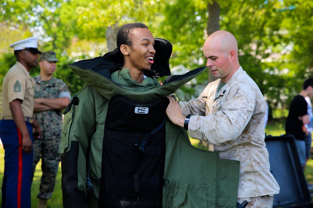 Staff Sgt. Adam Morris, an explosive ordnance disposal technician, helps a high school student try on an EOD bomb suit during a Marine Air Ground Task Force demonstration at Massapequa High School in Long Island, New York. The Marines are visiting the city to interact with the public, demonstrate capabilities and teach the people of New York about America's sea services.