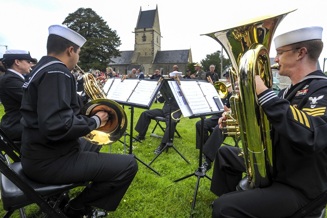 Members of the U.S. Naval Forces Europe Band Brass Quintet play music outside the church where Kenneth Moore and Robert Wright provided medical care to 80 combatants and one child during World War II in Angoville au Plain, France, June 4, 2016. Moore and Wright were combat medics assigned to the 101st Airborne Division who provided care to both allies and enemies as long as they respected their wishes and left their weapons outside of the church so as not to compromise the status of the location as a noncombatant facility. Air Force photo by Staff Sgt. Timothy Moore