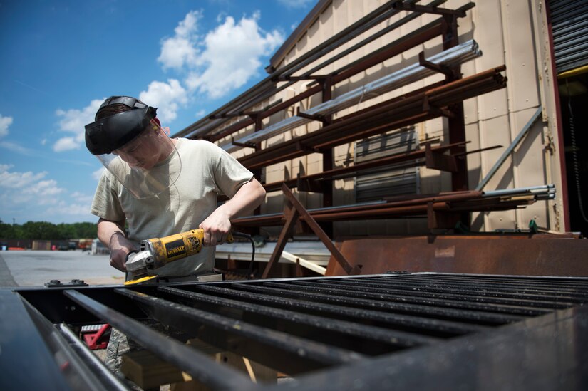 Senior Airman Michael Studer, 11th Civil Engineer Squadron structural journeyman, sands down welding points to a base gate outside the metal workshop on Joint Base Andrews, Md., June 1, 2016. The structures section of the 11th CES works with metal and wood projects that focus on preventive maintenance, lock jobs and repairs throughout base. (U.S. Air Force photo by Airman 1st Class Philip Bryant)