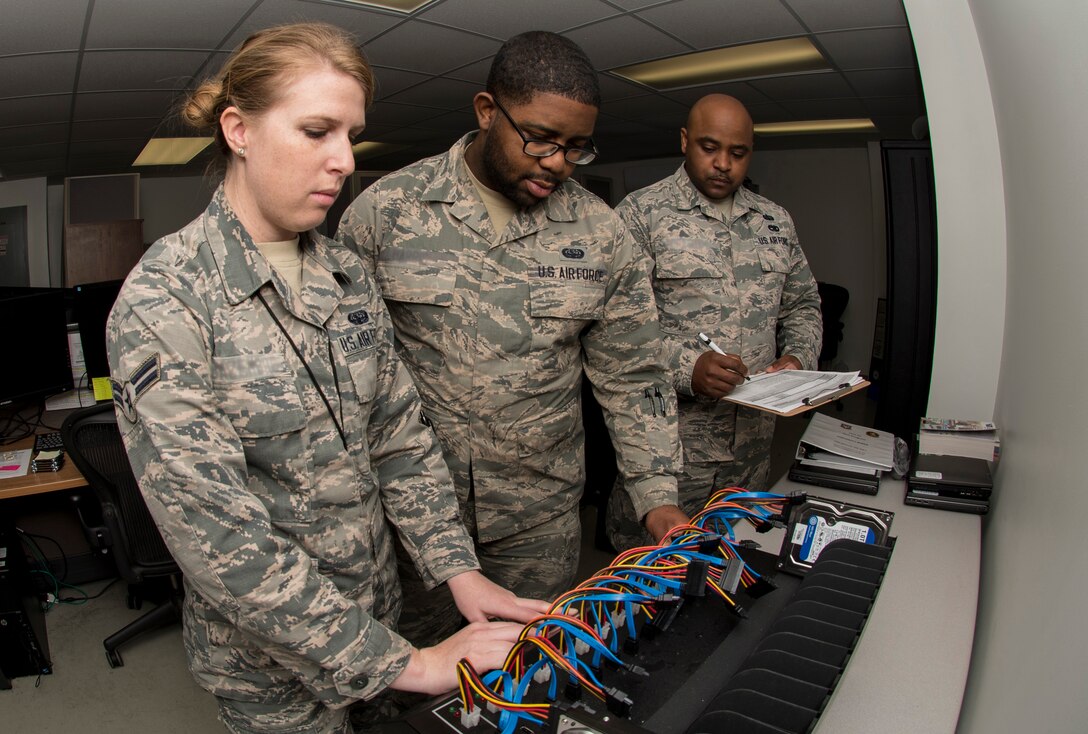 U.S. Air Force Staff Sgt. Tajwalid, quality assurance officer for the 363rd Intelligence, Surveillance and Reconnaissance Wing, evaluates Airmen 1st Class Jenny and William, cyber systems operators assigned to the 363rd Intelligence Support Squadron, as they perform tasks for cloning hard drives at Langley Air Force Base, Va., May 24, 2016. Cyber system operators must quickly respond to service outages and interruptions to network operations. (U.S. Air Force photo by Airman 1st Class Derek Seifert)
