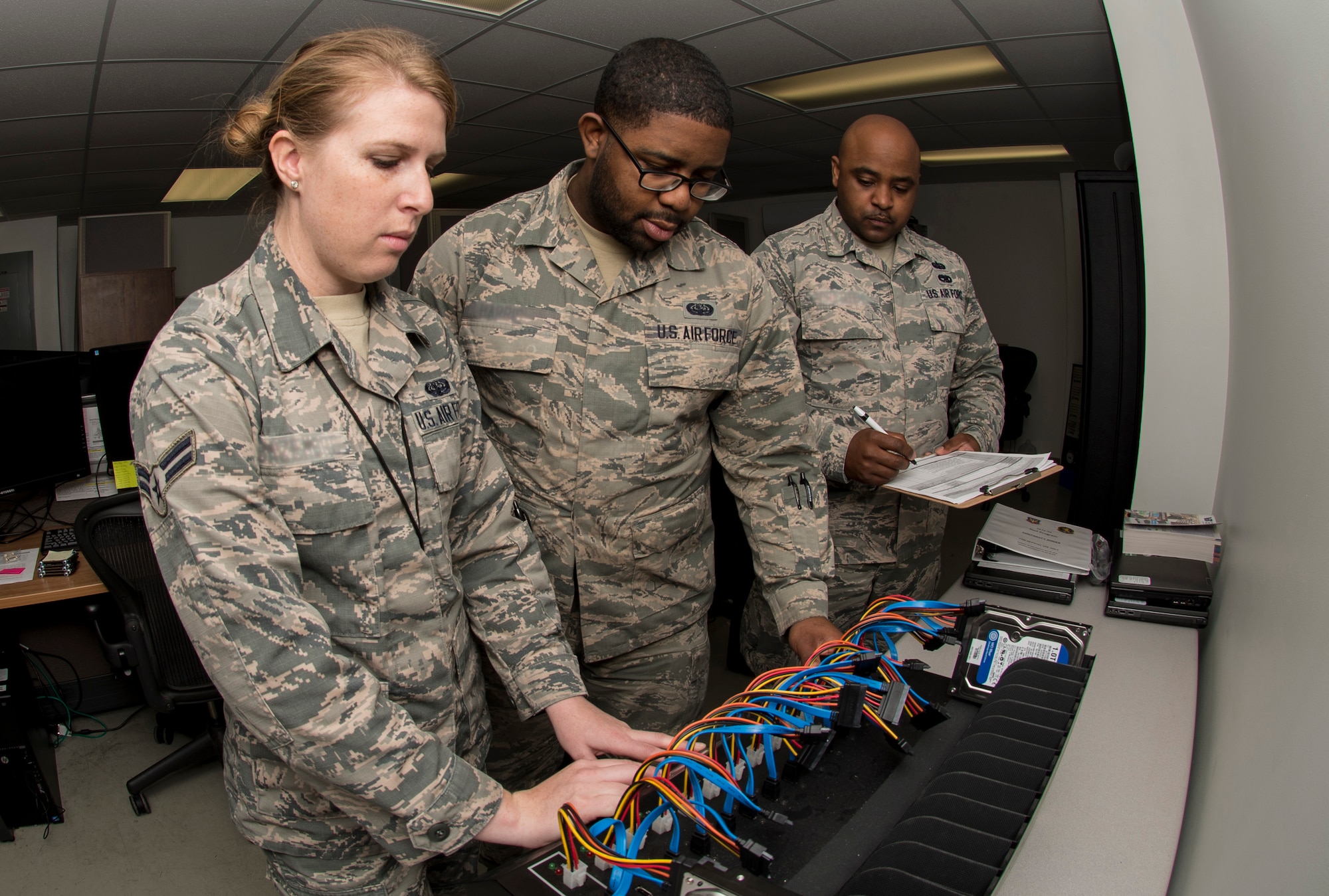 U.S. Air Force Staff Sgt. Tajwalid, quality assurance officer for the 363rd Intelligence, Surveillance and Reconnaissance Wing, evaluates Airmen 1st Class Jenny and William, cyber systems operators assigned to the 363rd Intelligence Support Squadron, as they perform tasks for cloning hard drives at Langley Air Force Base, Va., May 24, 2016. Cyber system operators must quickly respond to service outages and interruptions to network operations. (U.S. Air Force photo by Airman 1st Class Derek Seifert)
